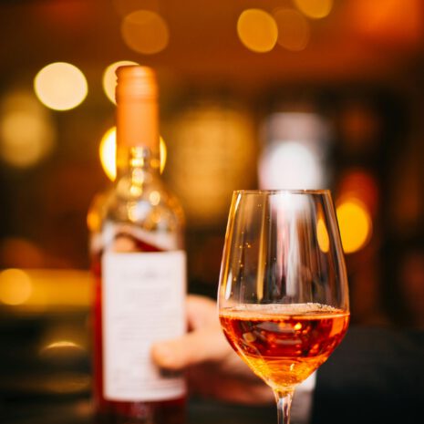 Accord mets et vins - L'Expérience Signature ARIA Paris Verre de vin rosé et bouteille tenue en main dans une lumière tamisée et chaleureuse, restaurant ARIA Paris