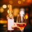 Verre de vin rosé et bouteille tenue en main dans une lumière tamisée et chaleureuse, restaurant ARIA Paris