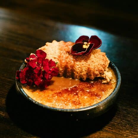 La Brûlée — Crème brûlée et fleurs comestibles, ARIA Paris Crème brûlée caramel doré, tuile croustillante et fleurs comestibles dans un bol noir, restaurant ARIA Paris