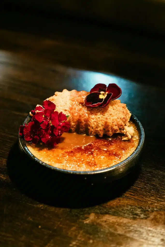 Crème brûlée caramel doré, tuile croustillante et fleurs comestibles dans un bol noir, restaurant ARIA Paris