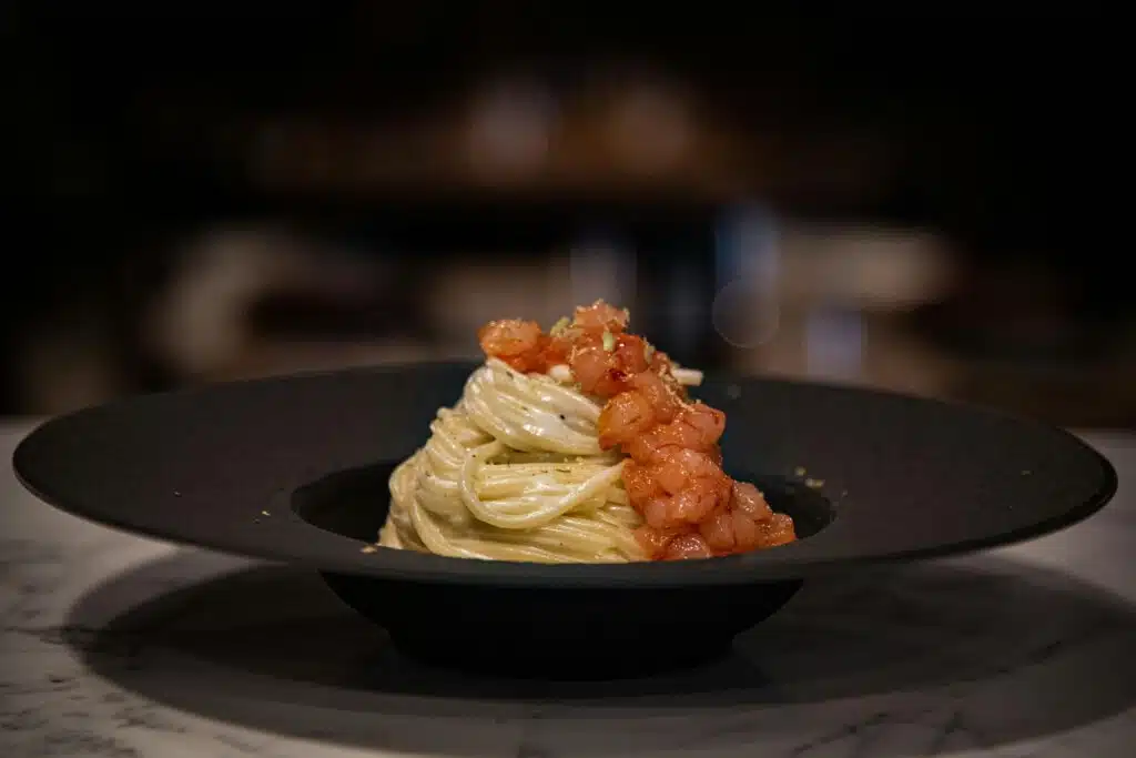 Spaghetti en nid avec gambas sautées et parmesan râpé dans un bol noir profond, restaurant ARIA Paris