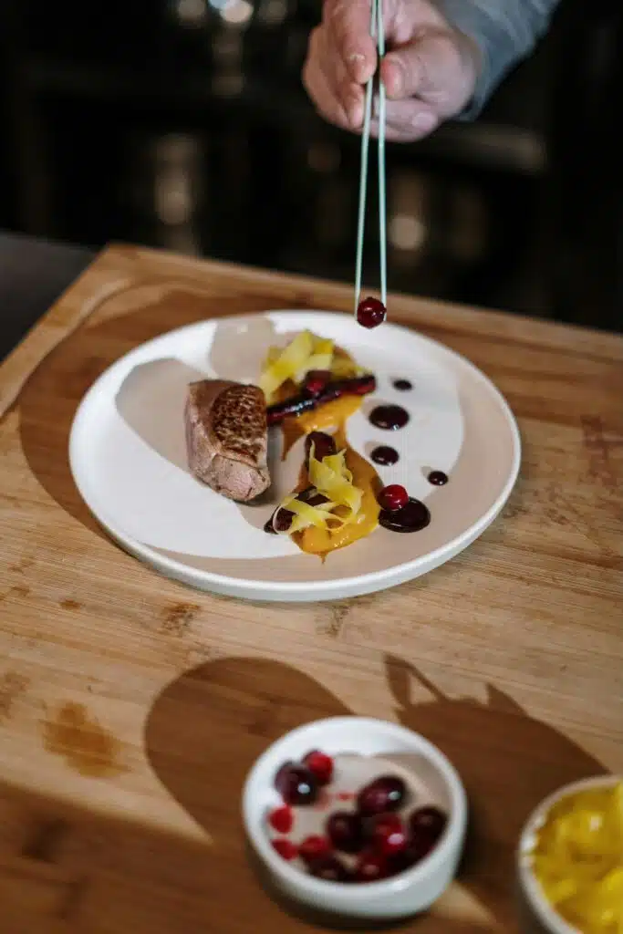 Chef Grabiel du restaurant fictif ARIA en train de dresser une assiette avec une pince à dresser.
